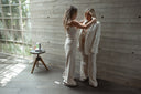 Two women in formal attire standing in a room with wooden walls and a small round table.